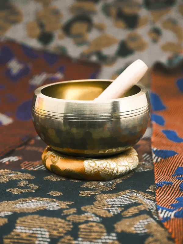 Bronze Nepali singing bowl with wooden striker and gold jacquard cushion on textured fabrics
