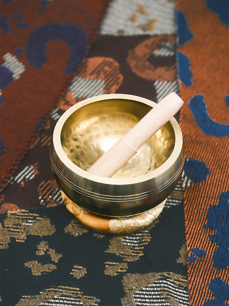 Top view bronze singing bowl with wooden striker and gold jacquard cushion