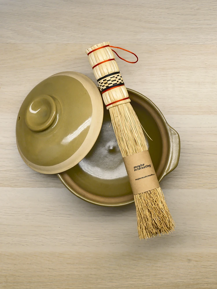 Natural sorghum pot brush resting on earthy tone ceramic pot